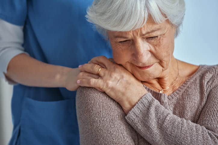 A nursing home nurse is holding the shoulder of a dementia patient, providing comfort.