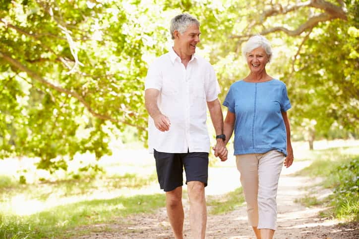Two elderly people walking while holding hands in the summer.