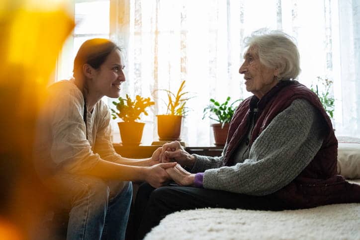 A mental health specialist smiling and holding hands with an elderly patient at an assisted living facility.