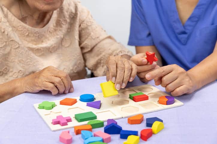 An Assisted Living Facility Nurse Completes A Puzzle With A Memory Care Patient.