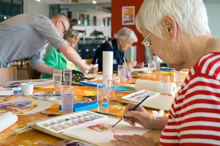 Seniors Participating In A Painting Class Together At An Assisted Living Facility.